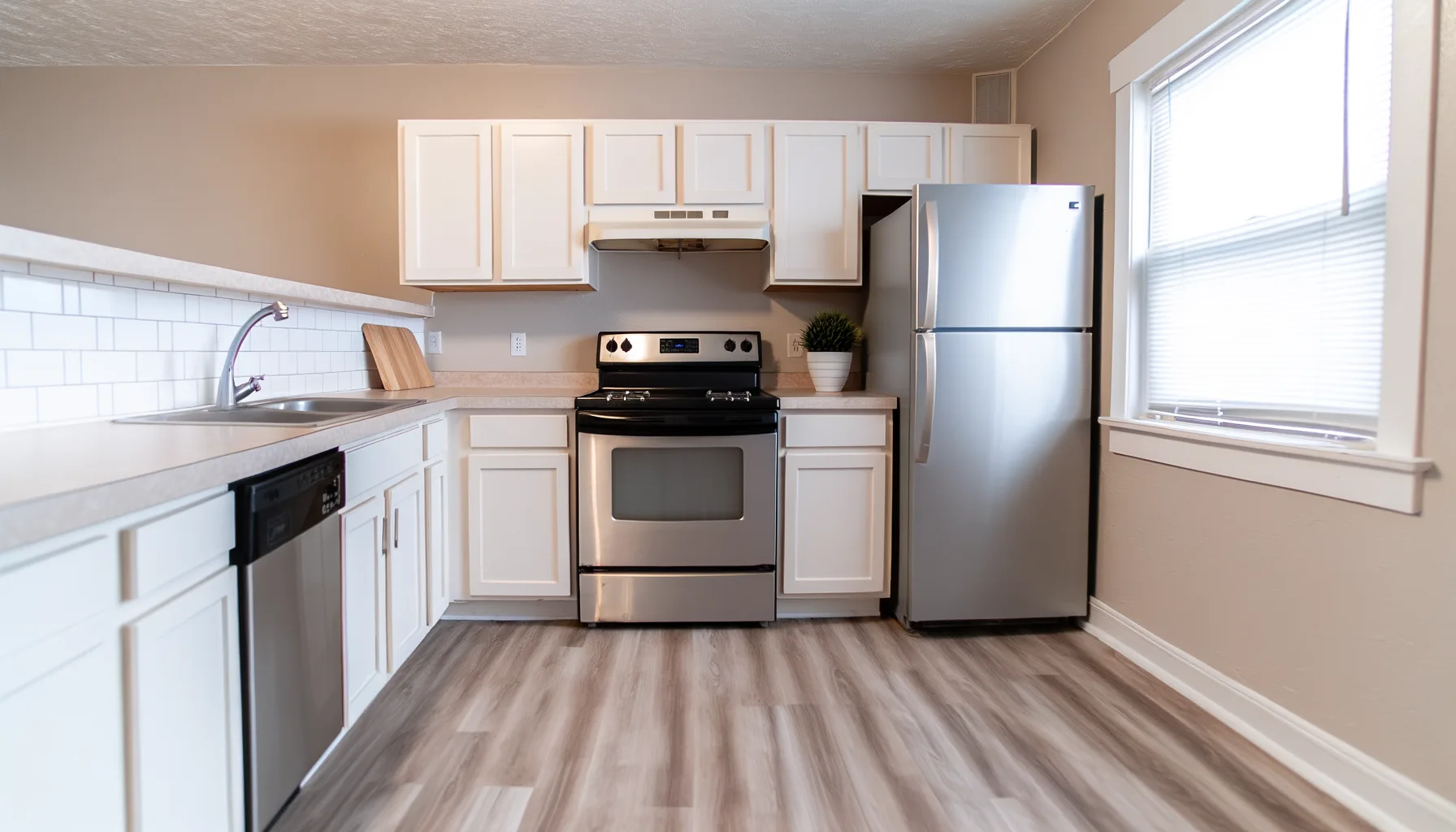 A modern residential kitchen in a Kansas City rental property featuring stainless steel appliances including a refrigerator, dishwasher, and range against neutral-toned walls and light wood or laminat